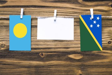Hanging flags of Palau and Solomon Islands attached to rope with clothes pins with copy space on...
