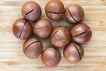 Inshell macadamia nuts in a heap in the center on a brown wooden surface, top view