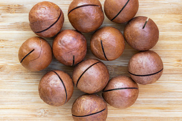 Twelve macadamia nuts lie in the center on a brown wooden surface, top view