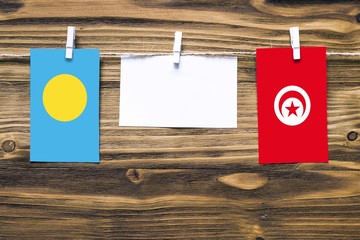 Hanging flags of Palau and Tunisia attached to rope with clothes pins with copy space on white note paper on wooden background.Diplomatic relations between countries.