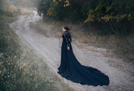 silhouette of gothic lady from old fantasy horror movie. Walks along the road in the autumn forest. Beautiful vampire. Black vintage dress with long train. design Old dark fashion. Halloween holiday