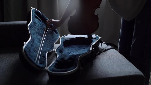 Man approaches the violin case, opens the case and pulls out his musical instrument close-up in slow motion. Musician is going to start playing the violin