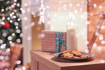 Beautiful Christmas gift with cookies and glass of milk for Santa Claus on table in room