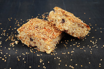 Homemade cake with sesame, nuts and chocolate on top on black wooden background