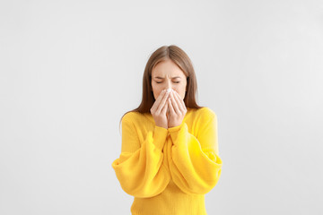 Young woman suffering from allergy on light background