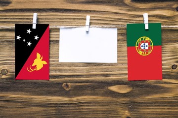 Hanging flags of Papua New Guinea and Portugal attached to rope with clothes pins with copy space on white note paper on wooden background.Diplomatic relations between countries.