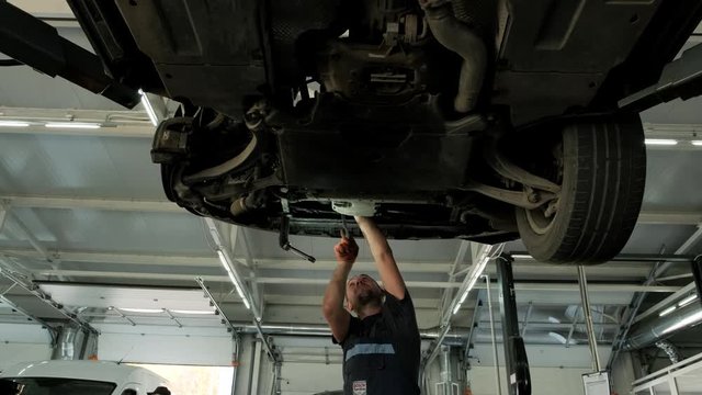 Auto mechanic working underneath car lifting machine at the garage. Auto repair shop, Car service, repair.   