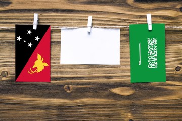Hanging flags of Papua New Guinea and Saudi Arabia attached to rope with clothes pins with copy space on white note paper on wooden background.Diplomatic relations between countries.