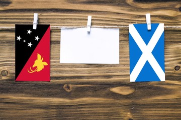 Hanging flags of Papua New Guinea and Scotland attached to rope with clothes pins with copy space on white note paper on wooden background.Diplomatic relations between countries.