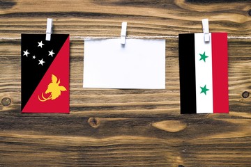 Hanging flags of Papua New Guinea and Syria attached to rope with clothes pins with copy space on...