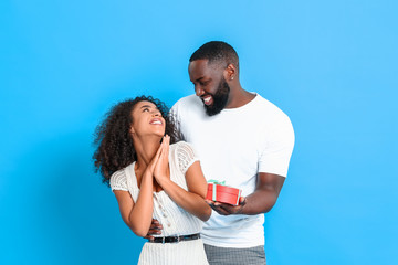 Portrait of African-American man giving present to his girlfriend on color background