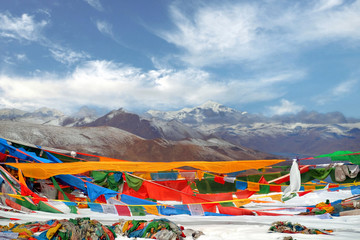 Tibetan praying flags in front of the Yamdrok Lake, reflecting the brown colors of Mt. Naiqinkangsang against a blue clear sky.