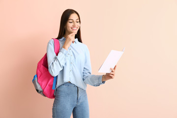 Portrait of teenage schoolgirl with book on color background