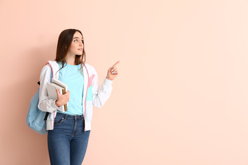 Portrait of teenage schoolgirl pointing at something on color background