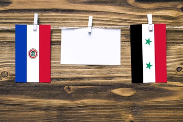 Hanging flags of Paraguay and Syria attached to rope with clothes pins with copy space on white...