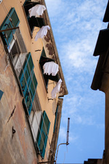 Fototapeta na wymiar Italy, Liguria region, Cinque Terra. Small street in old town, view from botton to the top. Blue sky, yellow walls and green shutters, white clothes drying on the ropes