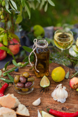 Delicious and romantic italian snack outside of a couple: wine, olives, bottle of olive oil, bread, fruits. Luxury lifestyle, healthy and gourmet food. Green background