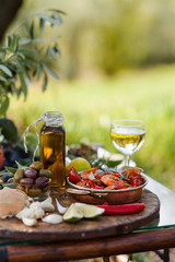 Romantic italian lunch outside for a couple: copper pan with delicious and spicy fried shrimps with herbs and garlic, wine, bread, olives. Bottle of olive oil. Luxury lifestyle, gourmet food
