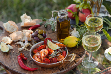 Romantic italian lunch outside of a couple: copper pan with delicious and spicy fried shrimps with herbs and garlic, wine, olives. Luxury lifestyle, gourmet food
