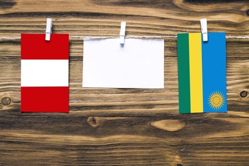 Hanging flags of Peru and Rwanda attached to rope with clothes pins with copy space on white note paper on wooden background.Diplomatic relations between countries.