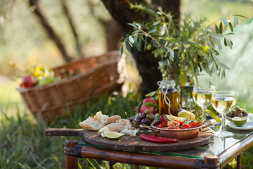 Romantic italian lunch outside of a couple: copper pan with delicious and spicy fried shrimps with herbs and garlic, wine, olives. Luxury lifestyle, gourmet food. Closeup