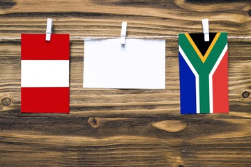 Hanging flags of Peru and South Africa attached to rope with clothes pins with copy space on white note paper on wooden background.Diplomatic relations between countries.