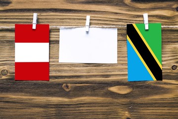 Hanging flags of Peru and Tanzania attached to rope with clothes pins with copy space on white note paper on wooden background.Diplomatic relations between countries.