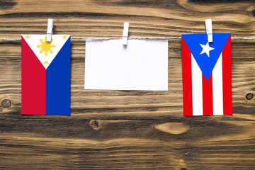 Hanging flags of Philippines and Puerto Rico attached to rope with clothes pins with copy space on white note paper on wooden background.Diplomatic relations between countries.