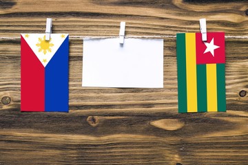 Hanging flags of Philippines and Togo attached to rope with clothes pins with copy space on white note paper on wooden background.Diplomatic relations between countries.