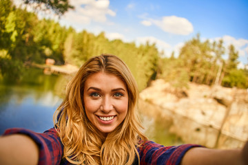 Female tourist exploring new places making a selfie photo. Portrait of handsome woman on nature near the lake at forest background.