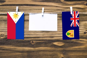 Hanging flags of Philippines and Turks And Caicos Islands attached to rope with clothes pins with copy space on white note paper on wooden background.Diplomatic relations between countries.