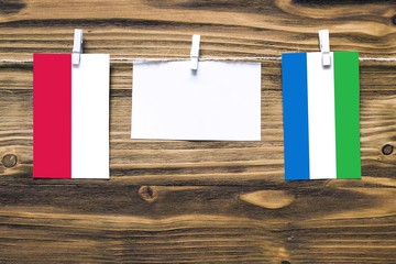 Hanging flags of Poland and Sierra Leone attached to rope with clothes pins with copy space on white note paper on wooden background.Diplomatic relations between countries.