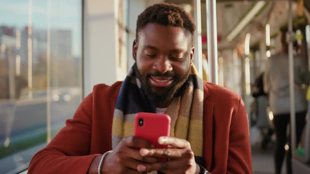 Portrait smiling young african american man use smartphone sitting in tram traffic typing at sunny day handsome passangers stylish transportation using way internet online texting guy slow motion