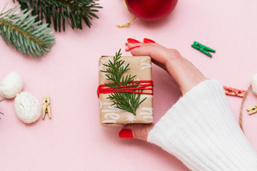 hand made, female hands with beautiful red manicure demonstrate a wrapped gift on a pink background