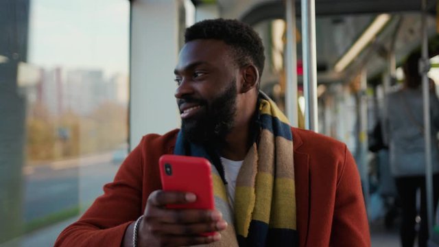 Face smiling young african american man use smartphone sitting in tram traffic typing at sunny day handsome passangers stylish transportation using way internet online texting portrait guy slow motion