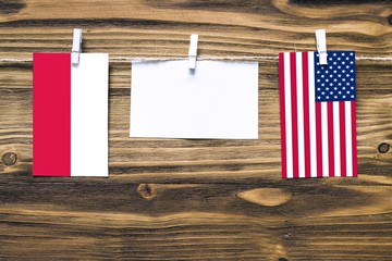 Hanging flags of Poland and United States attached to rope with clothes pins with copy space on white note paper on wooden background.Diplomatic relations between countries.