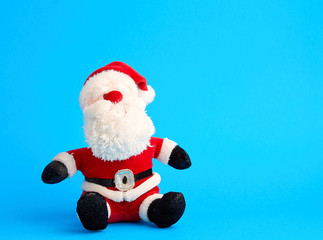 traditional toy santa claus in a red suit and white beard sits on a blue background