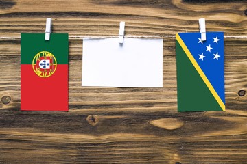 Hanging flags of Portugal and Solomon Islands attached to rope with clothes pins with copy space on white note paper on wooden background.Diplomatic relations between countries.