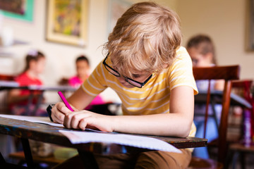 Blonde boy with glasses drawing. Group of elementary school pupils in classroom on art class....