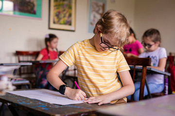 Blonde boy with glasses drawing. Group of elementary school pupils in classroom on art class. Russia, Krasnodar, May, 23, 2019