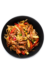 Sliced beef, noodles in sauce, vegetables and sesame seeds in a black plate isolated on white background