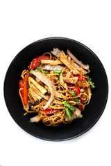 Sliced grilled chicken breast, noodles in sauce, vegetables and sesame seeds in a black plate isolated on white background