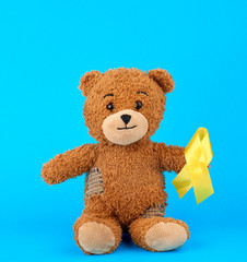brown teddy bear sits and holds in his paw a yellow silk ribbon on a blue background