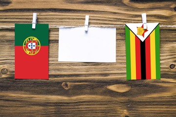 Hanging flags of Portugal and Zimbabwe attached to rope with clothes pins with copy space on white note paper on wooden background.Diplomatic relations between countries.