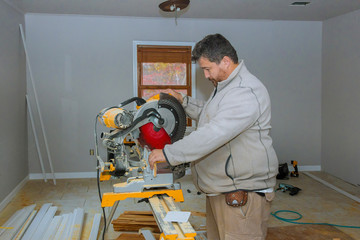 Worker cuts wood baseboard on the power saw