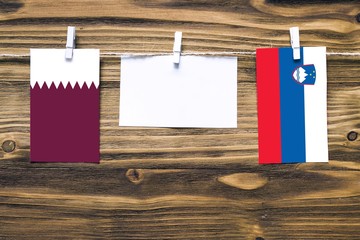 Hanging flags of Qatar and Slovenia attached to rope with clothes pins with copy space on white note paper on wooden background.Diplomatic relations between countries.