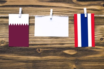 Hanging flags of Qatar and Thailand attached to rope with clothes pins with copy space on white note paper on wooden background.Diplomatic relations between countries.