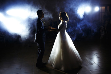First wedding dance of newlywed. Wedding couple dancing in the darkness. Groom holds bride's hand dancing with her in the middle of a restaurant. Happy bride and groom and their first dance. 