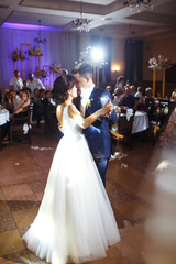 First wedding dance of newlywed. Groom holds bride's hand dancing with her in the middle of a restaurant. Touching and emotional first dance of the couple on their wedding with lights.