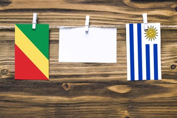 Hanging flags of Republic Of The Congo and Uruguay attached to rope with clothes pins with copy space on white note paper on wooden background.Diplomatic relations between countries.